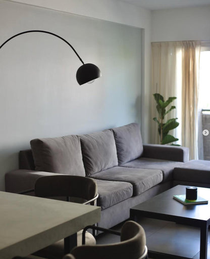 Sofá Elton gris con puff al tono, lámpara de arco negra y mesa ratona oscura, en el living de Simón decorado con WN Interiores