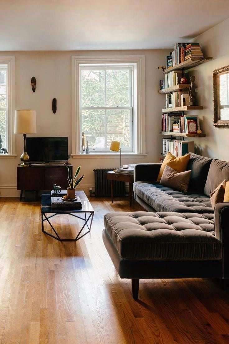 Sofá esquinero gris oscuro capitoné en living con piso de madera y biblioteca flotante – Tienda de Banquitos