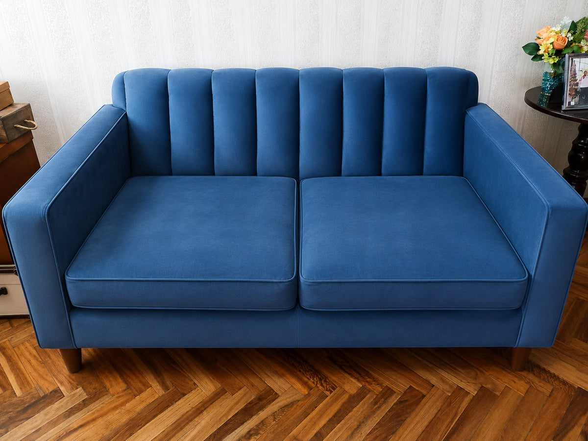 Sofá Mila de dos cuerpos en azul océano, con respaldo acanalado vertical y patas de madera, en el living de Juliana