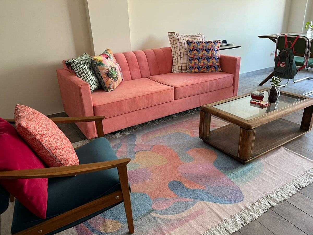 Sofá Mila en color coral en el living de Mari, con almohadones estampados, alfombra en tonos pastel y mesa ratona de madera y vidrio