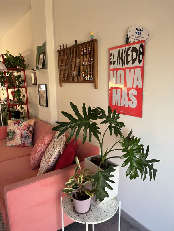 Lateral del Sofá Mila coral junto a plantas y un póster rojo en la pared del living de Mari