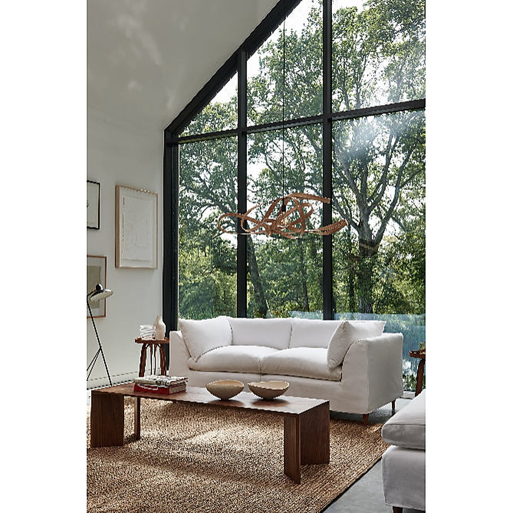 Sofá Orlando con funda blanca en living de doble altura con ventanal y mesa ratona de madera - Tienda de Banquitos