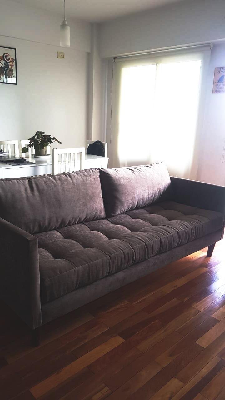Sofá Ristretto gris topo con asiento capitoné y apoyabrazos finos, en el living-comedor de Mariano con piso de madera