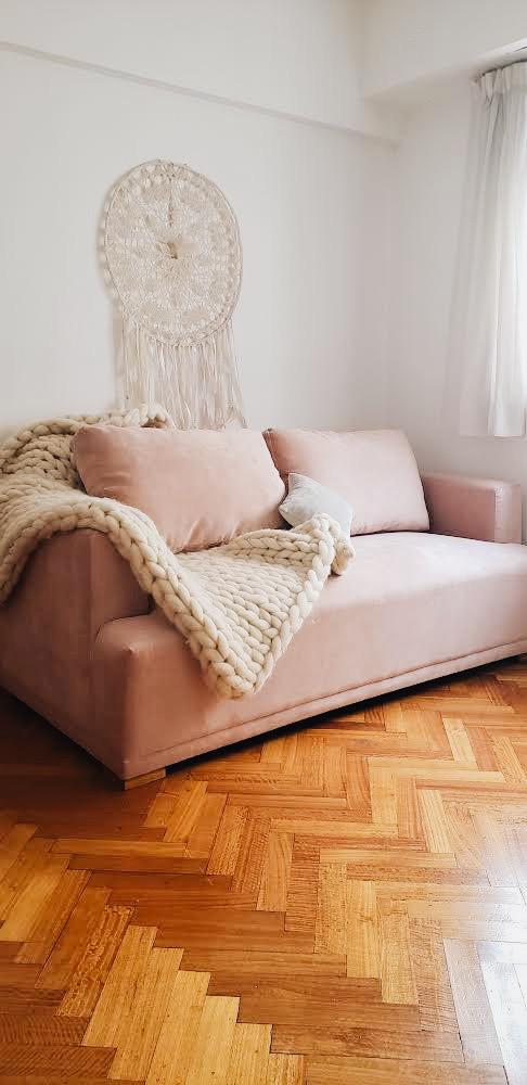 Sofá rosa de Cecilia con almohadones de respaldo sueltos, apoyabrazos bajos y una manta tejida gruesa