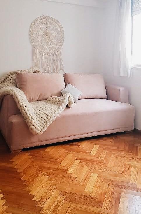 Sofá rosa a medida de líneas rectas, con manta tejida gruesa, sobre el parquet espina de pez del living boho de Cecilia