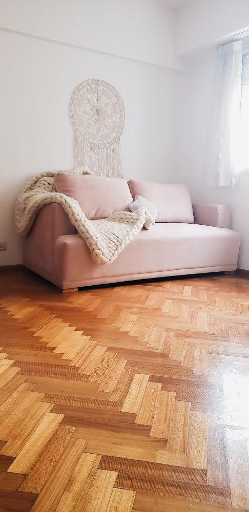 Vista general del sofá rosa a medida de Cecilia, con un atrapasueños de macramé en la pared y parquet espina de pez