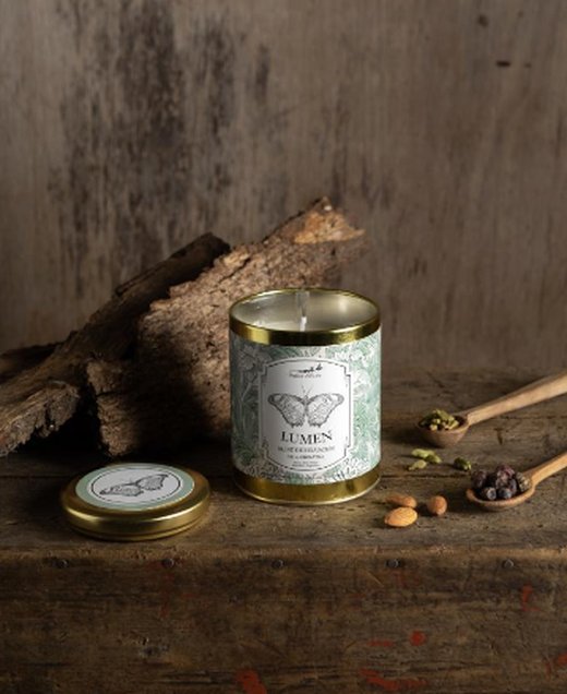 Vela aromática Lumen de Petite Affaire con etiqueta de mariposa junto a su tapa, cardamomo y almendras