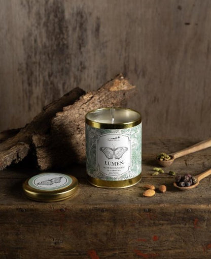 Vela aromática Lumen de Petite Affaire con etiqueta de mariposa junto a su tapa, cardamomo y almendras