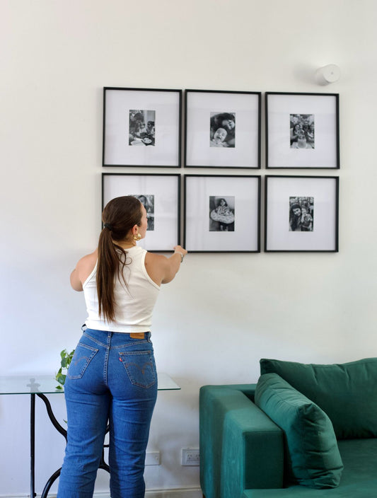 Una mujer acomoda los cuadros en blanco y negro sobre el Esquinero Magnolia verde, en el proyecto de WN Interiores