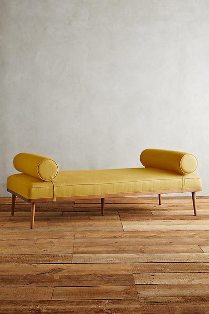 Banqueta estilo escandinavo con almohadones cilíndrico doble y patas de madera. Minimalista y funcional, perfecta para ambientes acogedores.