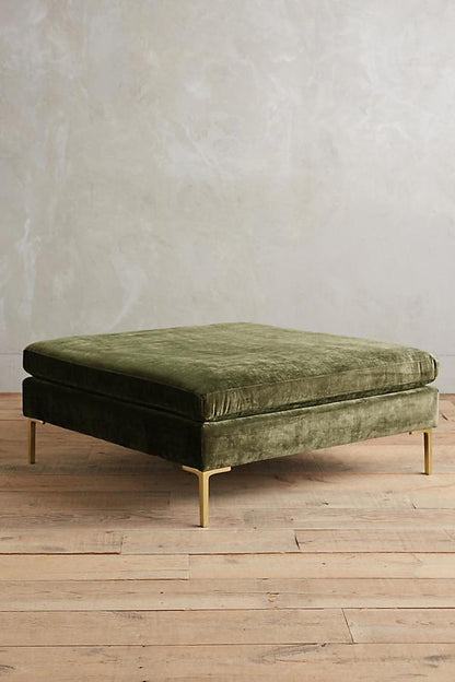 Banqueta rectangular tapizada en con patas doradas. Su diseño compacto y moderno la vuelve ideal para espacios reducidos o como apoya pies.