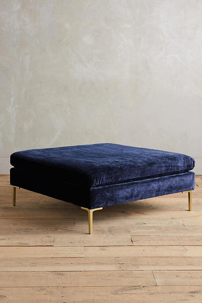 Banqueta rectangular tapizada en con patas doradas. Su diseño compacto y moderno la vuelve ideal para espacios reducidos o como apoya pies.