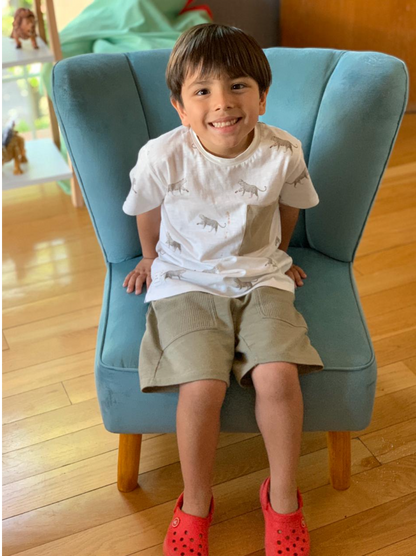 Niño sentado en un sillón azul con respaldo ancho y líneas suaves, destacado en el centro de la imagen