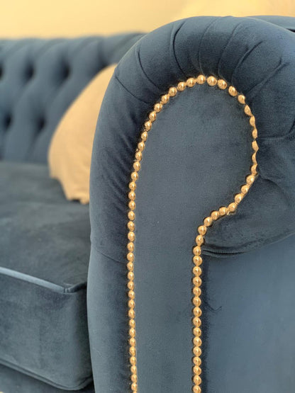 Juego de sillones con tapizado capitoné en tonos azul marino y gris, de diseño elegante y clásico, ubicados en un living luminoso con decoración sofisticada
