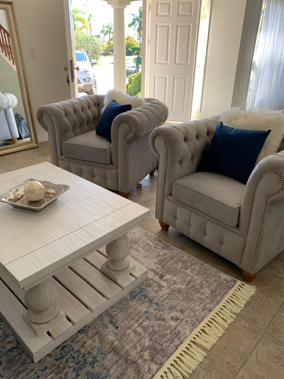 Juego de sillones con tapizado capitoné en tonos azul marino y gris, de diseño elegante y clásico, ubicados en un living luminoso con decoración sofisticada
