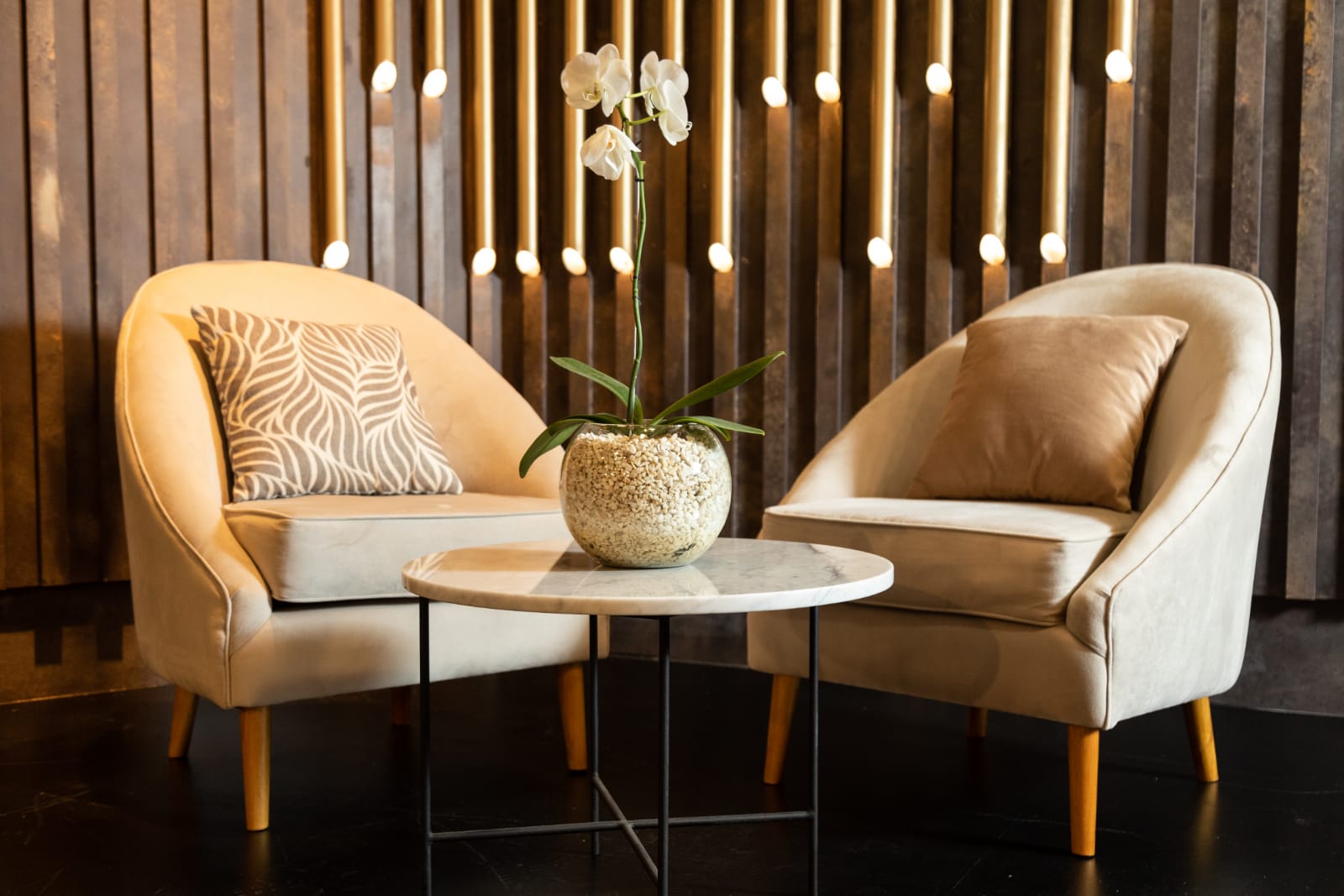 Par de sillones individuales tapizados en tono beige con patas de madera, de diseño moderno y respaldo curvo, decorados con almohadones a tono, ideales para un ambiente elegante y acogedor