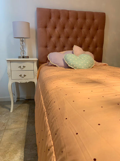 Respaldo de cama tapizado en terciopelo color terracota con diseño capitoné, acompañado de almohadones decorativos en tonos pastel y mesa de luz blanca con lámpara