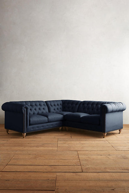 Sillón esquinero estilo Chesterfield en pana azul con capitoné, brazos curvos y patas altas. Clásico inglés con personalidad.