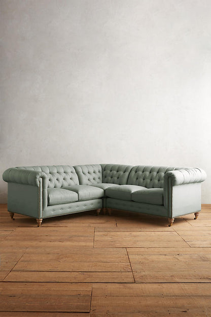 Sillón esquinero estilo Chesterfield en pana gris con capitoné, brazos curvos y patas altas. Clásico inglés con personalidad.