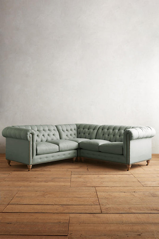 Sillón esquinero estilo Chesterfield en pana gris con capitoné, brazos curvos y patas altas. Clásico inglés con personalidad.
