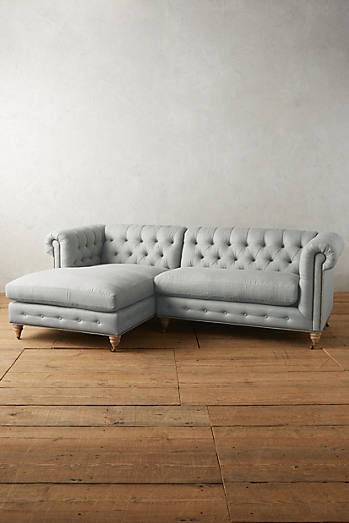 Sillón esquinero estilo Chesterfield en pana gris claro con capitoné, brazos curvos y patas altas. Clásico inglés con personalidad.