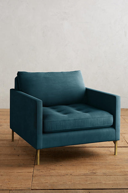 Sillón individual moderno en color azul con respaldo y asiento acolchados, apoyabrazos rectos y patas metálicas finas en dorado, sobre fondo blanco.