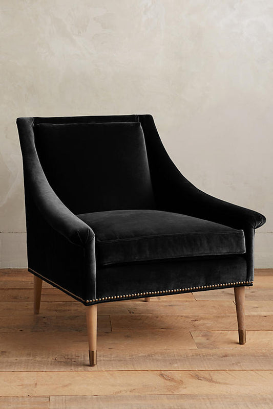 Sillón individual tapizado en negro, de líneas rectas con respaldo y asiento acolchados, brazos delgados y patas de madera rectas con detalle de tachas decorativas en la parte inferior.