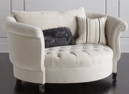Sillón redondo de estilo elegante en color crema, con respaldo curvo envolvente, apoyabrazos enrollados y asiento capitoné, patas cortas de madera.