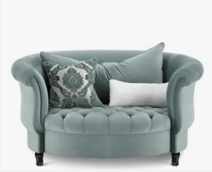 Sillón redondo de estilo elegante en color verde aqua, con respaldo curvo envolvente, apoyabrazos enrollados y asiento capitoné, patas cortas de madera.