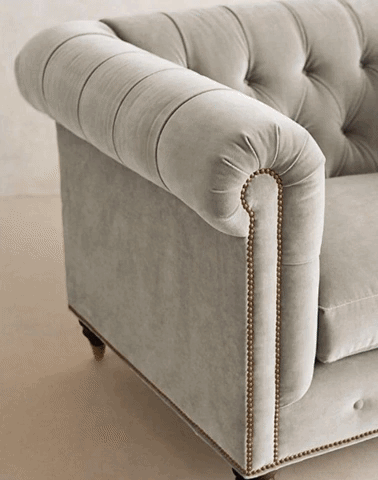 Sillón individual estilo Chesterfield tapizado, con capitoné en respaldo y apoyabrazos, tachas decorativas y patas de madera torneadas.