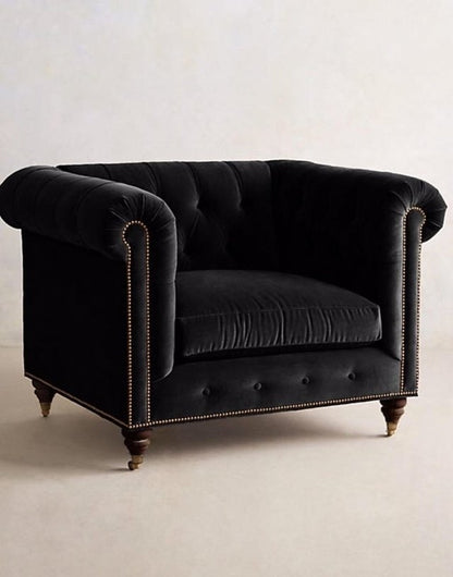 Sillón individual estilo Chesterfield tapizado en color negro, con capitoné en respaldo y apoyabrazos, tachas decorativas y patas de madera torneadas.