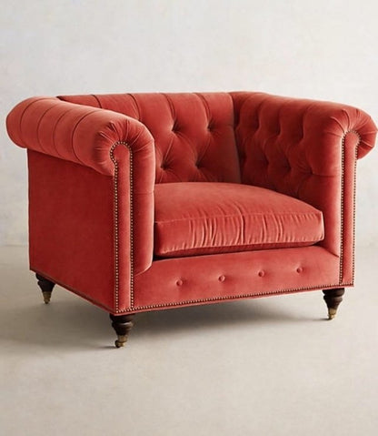 Sillón individual estilo Chesterfield tapizado en color rojo, con capitoné en respaldo y apoyabrazos, tachas decorativas y patas de madera torneadas.