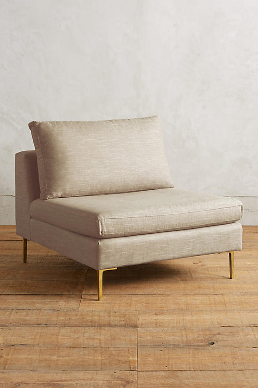 Módulo de sillón sin apoyabrazos en color crema, con respaldo alto y almohadón mullido, patas metálicas delgadas en tono dorado, sobre fondo blanco.