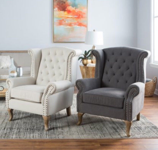 Sillón estilo clásico, con respaldo capitoné alto, orejas curvas, apoyabrazos redondeados y tachas decorativas, patas de madera talladas