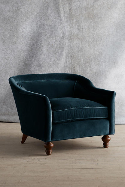 Sillón individual tapizado en color petroleo, con diseño de respaldo envolvente, asiento amplio y patas torneadas de madera oscura.