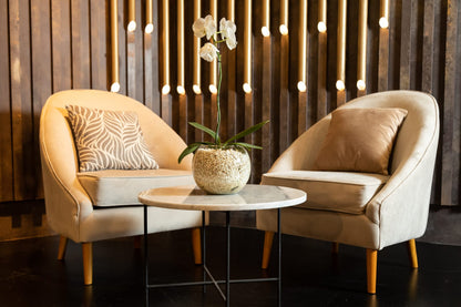 Par de sillones individuales tapizados en tono beige con patas de madera, de diseño moderno y respaldo curvo, decorados con almohadones a tono, ideales para un ambiente elegante y acogedor