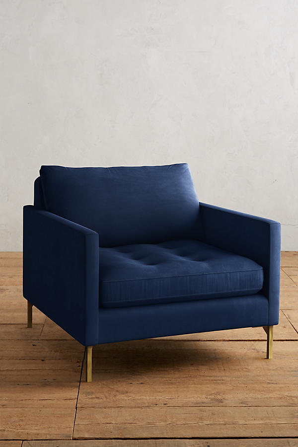 Sillón individual moderno en color azul con respaldo y asiento acolchados, apoyabrazos rectos y patas metálicas finas en dorado, sobre fondo blanco.
