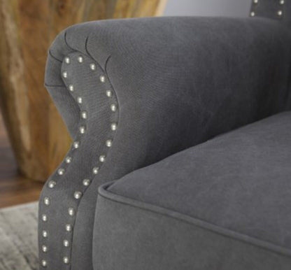 Sillón estilo clásico tapizado en color gris oscuro, con respaldo capitoné alto, orejas curvas, apoyabrazos redondeados y tachas decorativas, patas de madera talladas