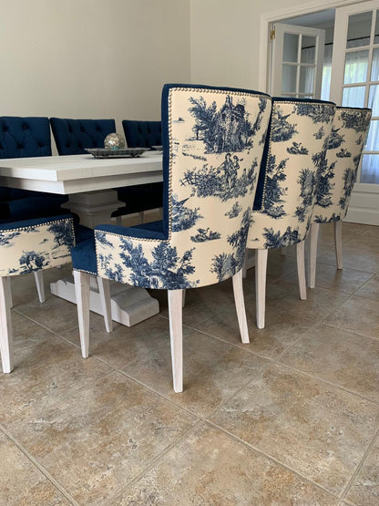 Silla de comedor tapizada en tela estampada blanca con diseño en azul, bordeada con detalles de tachas decorativas y patas de madera en tono claro
