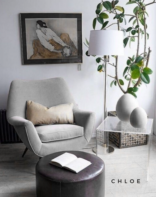 Sillón individual tapizado en gris, de diseño retro con respaldo curvo envolvente, asiento acolchonado y patas de madera inclinadas estilo escandinavo.