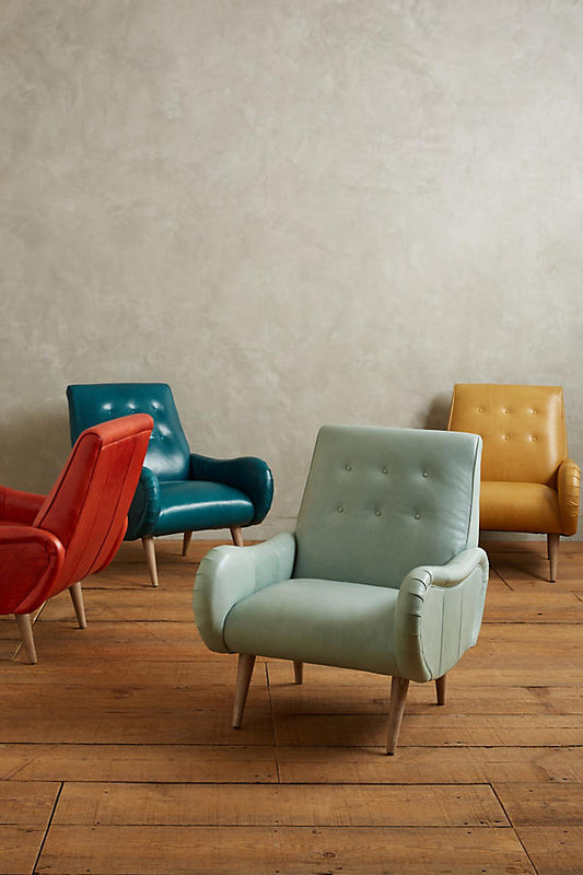 Sillón de un cuerpo estilo retro, con respaldo bajo capitoné, apoyabrazos curvos y patas de madera cónicas.