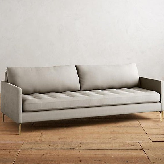 Sillón Ristretto de dos cuerpos con respaldo de almohadones sueltos, asiento tapizado capitoné y patas finas metálicas doradas. Diseño moderno y elegante con detalles clásicos.