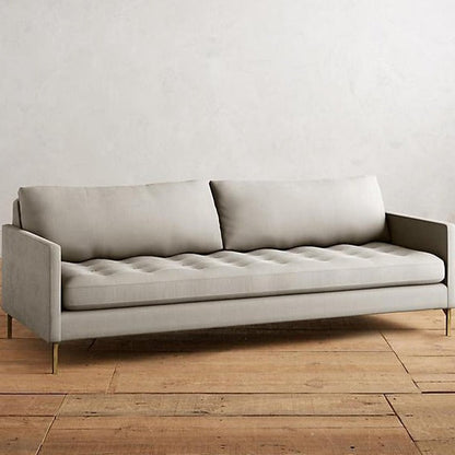 Sillón Ristretto de dos cuerpos con respaldo de almohadones sueltos, asiento tapizado capitoné y patas finas metálicas doradas. Diseño moderno y elegante con detalles clásicos.