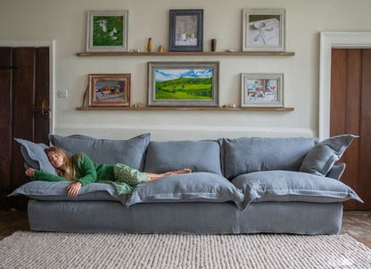 Sofá Comfy enfundado, con respaldo y apoyabrazos integrados, amplios cojines extra mullidos en asiento y respaldo, líneas suaves y estructura de base baja, presentado sobre fondo blanco, ideal para livings contemporáneos o espacios de descanso que buscan máxima comodidad y estilo relajado.