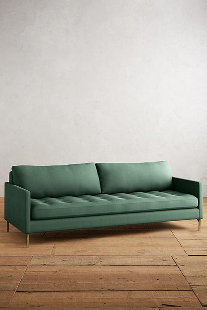 Sillón Ristretto de dos cuerpos con respaldo de almohadones sueltos, asiento tapizado capitoné y patas finas metálicas doradas. Diseño moderno y elegante con detalles clásicos.