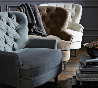 Sillón clásico tapizado con respaldo capitoné curvo, asiento acolchado y patas de madera cónicas.