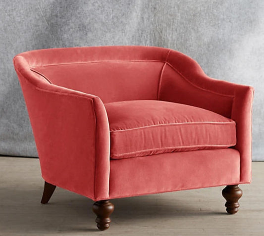 Sillón individual tapizado en color rosa, con diseño de respaldo envolvente, asiento amplio y patas torneadas de madera oscura.
