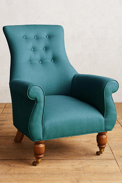 Sillón individual estilo clásico tapizado en aqua, con respaldo alto capitoné, apoyabrazos curvos y patas torneadas de madera.
