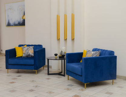 Sillón de un cuerpo tapizado en azul, con respaldo recto acanalado, apoyabrazos rectangulares y base baja con patas doradas.