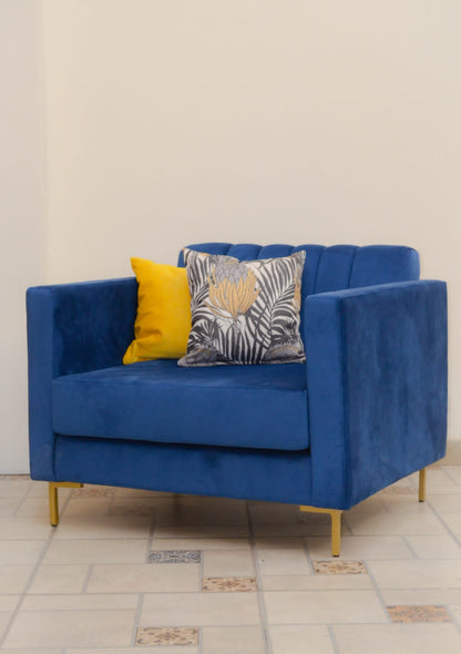 Sillón de un cuerpo tapizado en azul, con respaldo recto acanalado, apoyabrazos rectangulares y base baja con patas doradas.